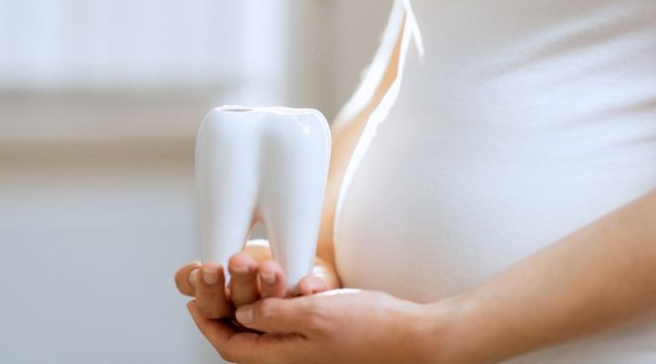 Mujer posa con diente preocupada por su salud bucodental y el embarazo - Dentista en Cuenca - Millán